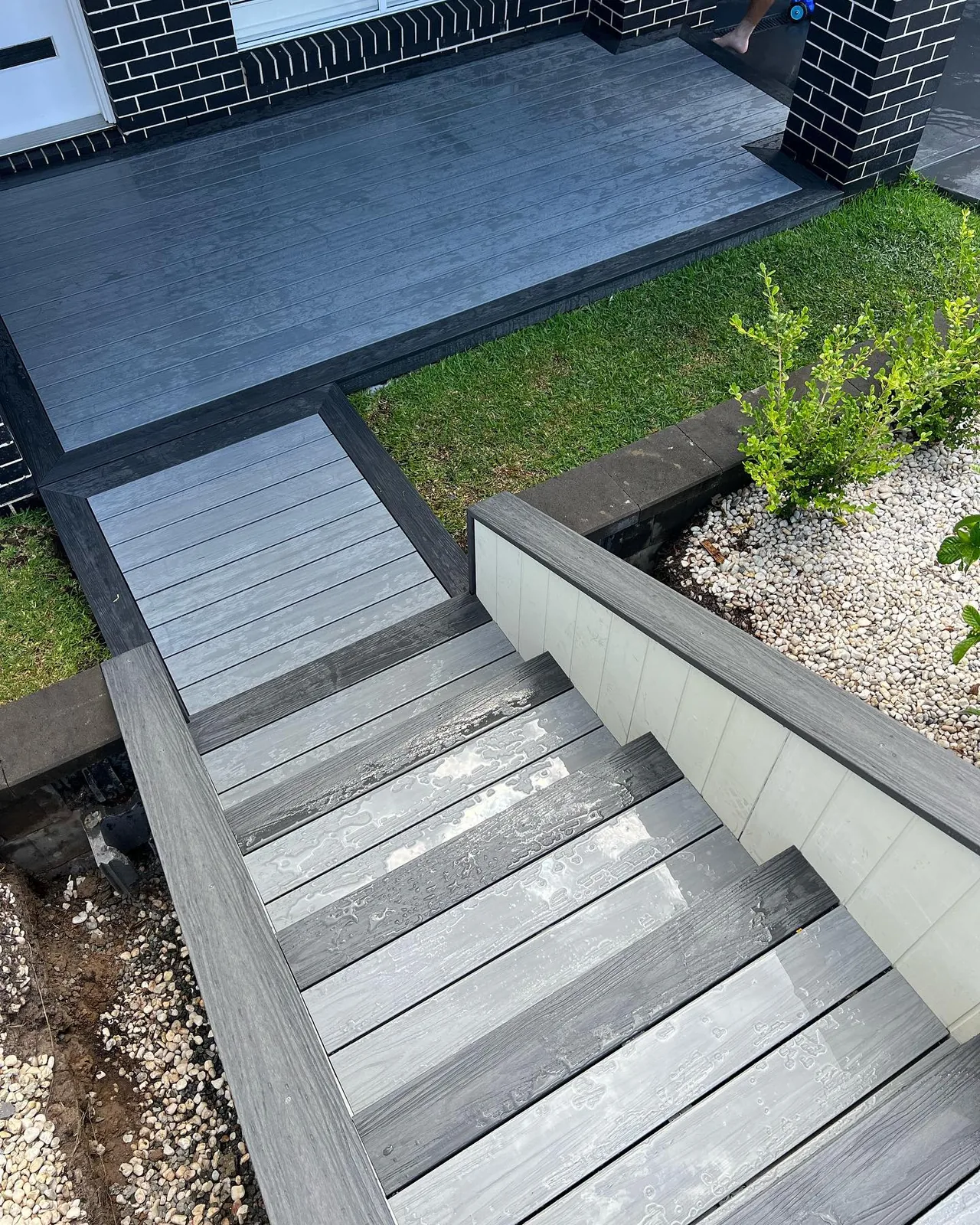 Grey composite entry decking and broad steps beside a dark brick home.