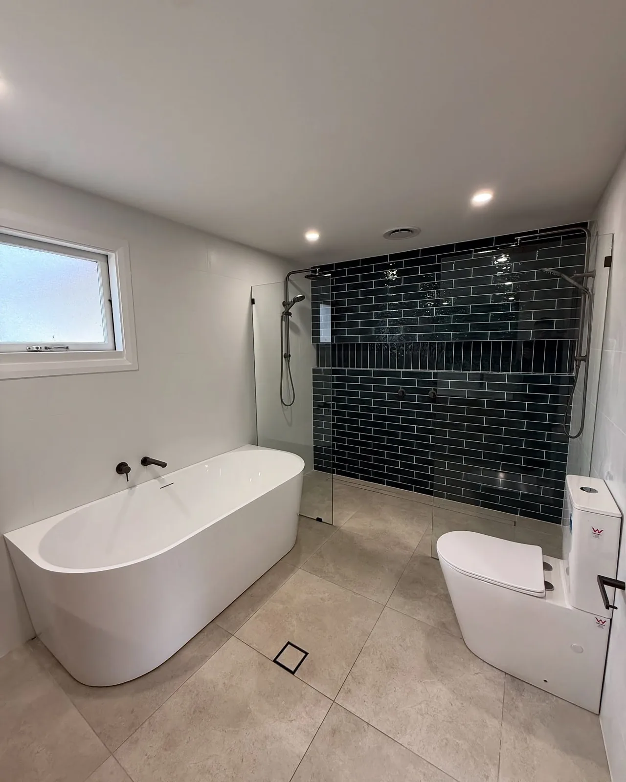 A white freestanding bath beside a glass shower with dark subway tiles.