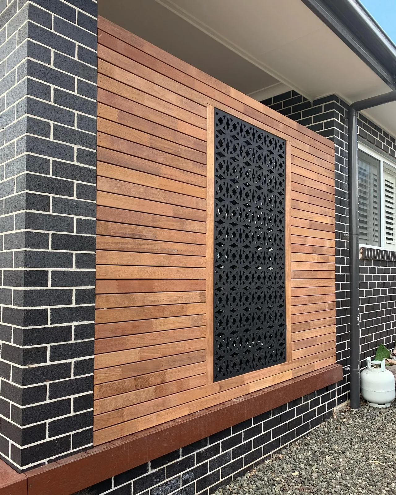 Timber privacy screening with a decorative dark lattice panel between brick pillars.