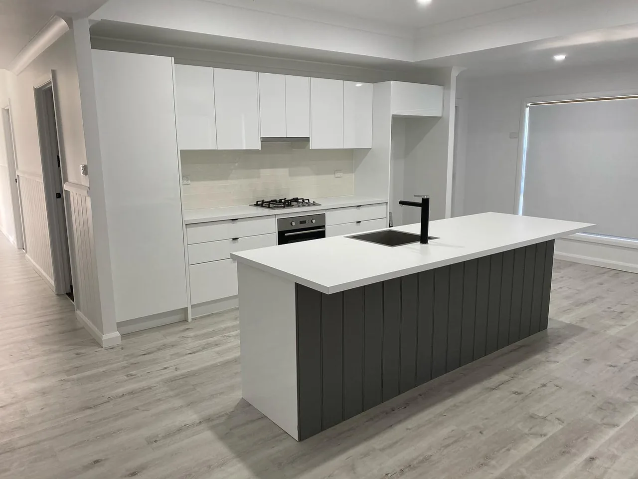 Open-plan white kitchen with a large dark-panelled island and black tapware.