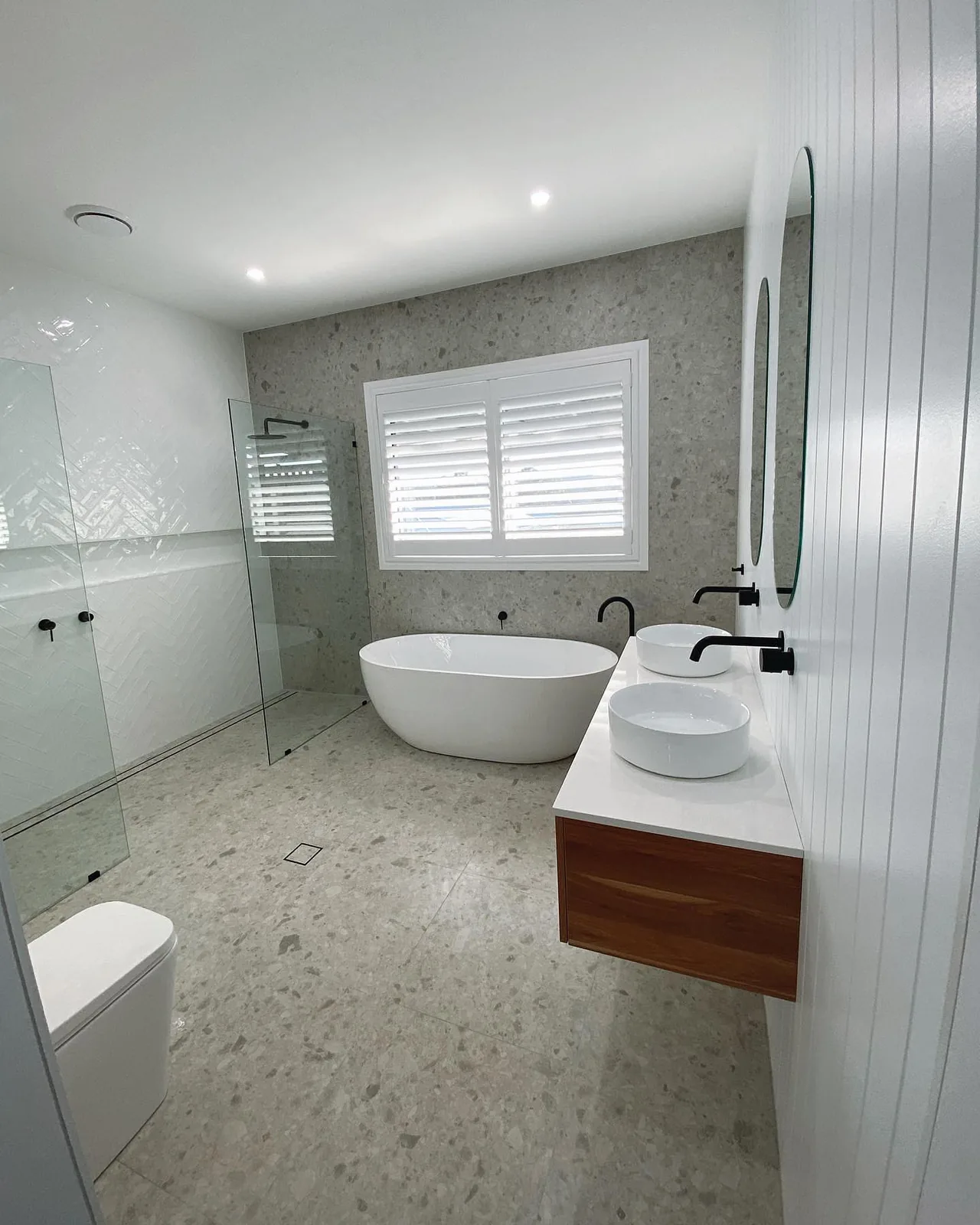 A bright bathroom with twin vessel basins, a freestanding bath and terrazzo flooring.