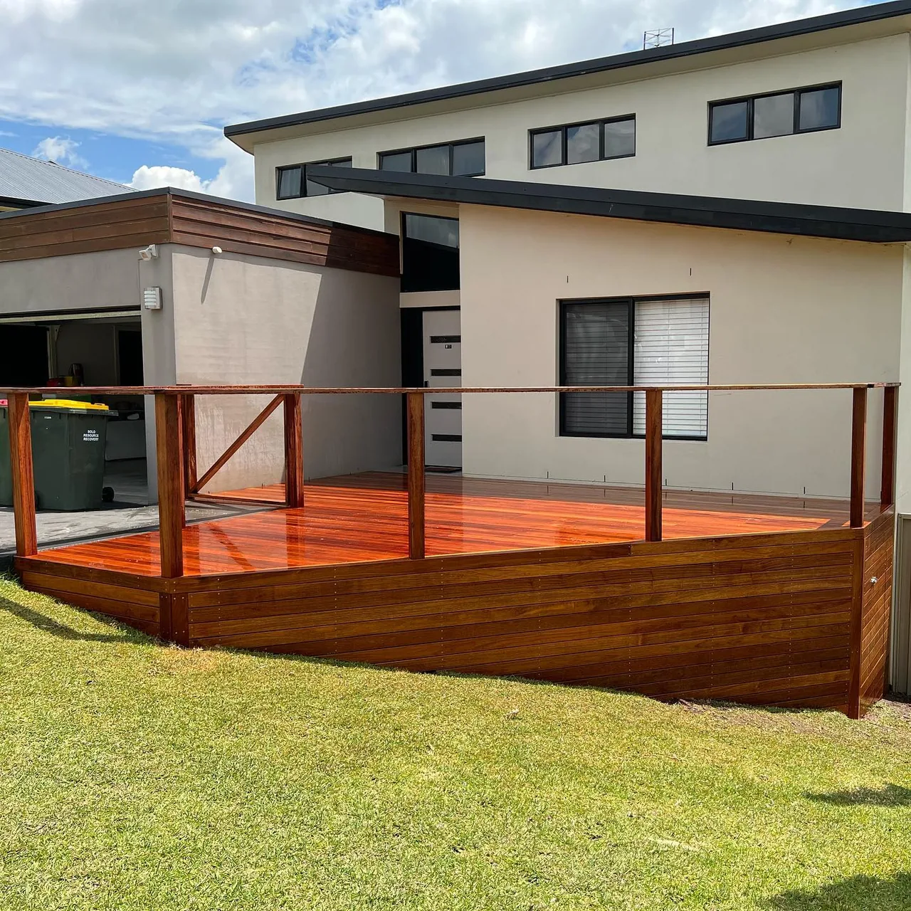 A polished timber deck and balustrade outside a contemporary two-storey home.