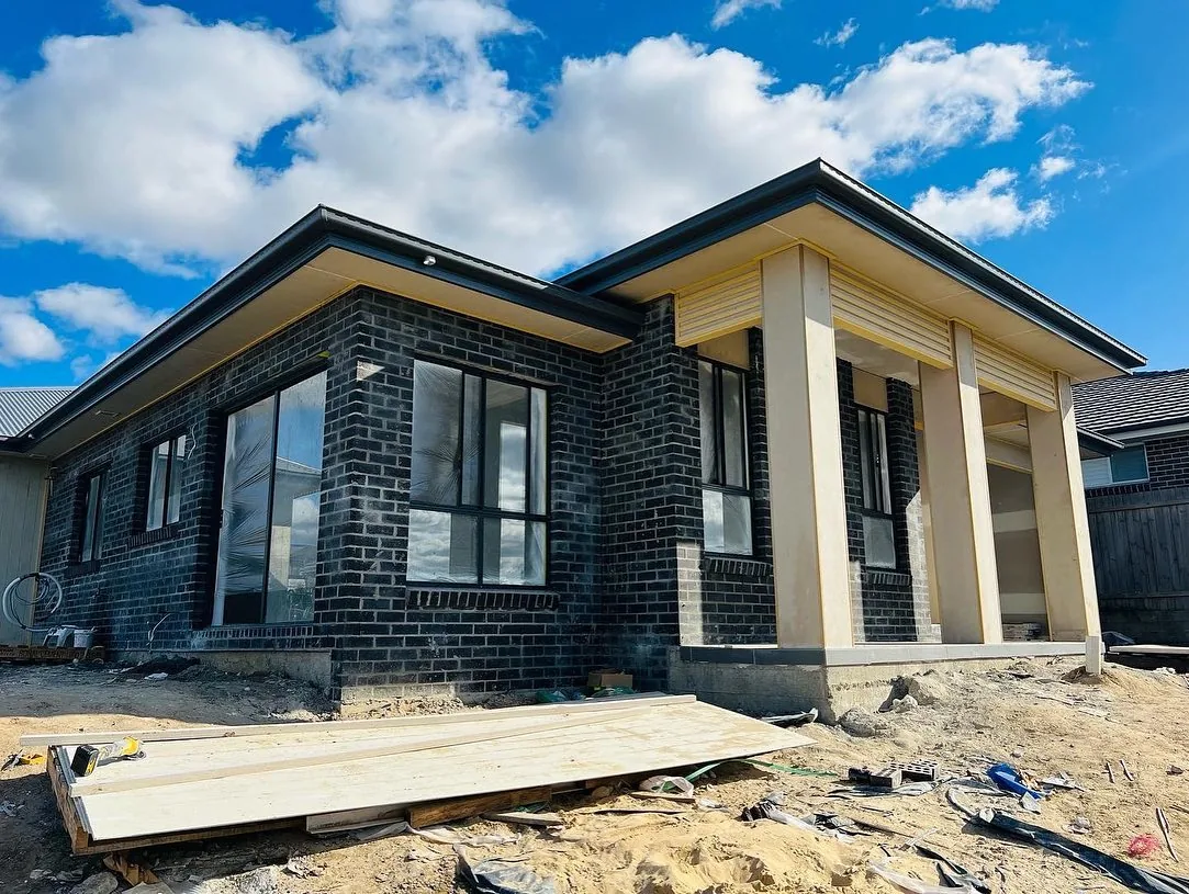 A contemporary dark brick home under construction, with a tall sheltered entry.