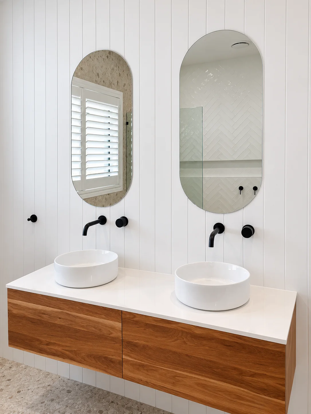 A timber bathroom vanity with two white basins, black wall taps and arched mirrors.