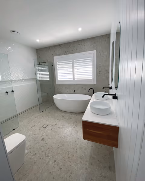 A bright bathroom with twin vessel basins, a freestanding bath, glass shower and timber vanity.