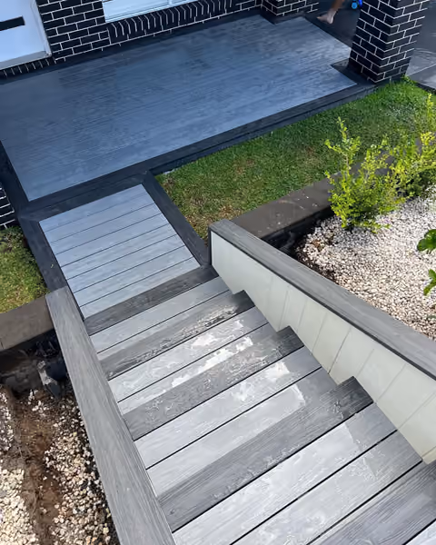 Grey composite entry decking and broad steps beside a dark brick home.