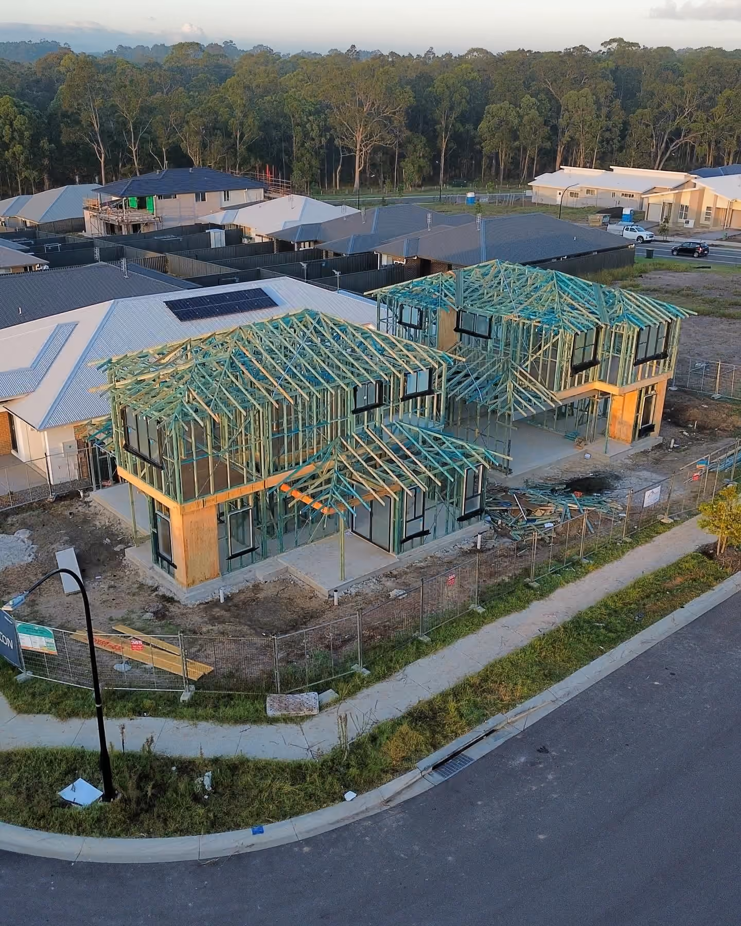 Aerial view of two neighbouring two-storey homes with wall framing and roof trusses under construction.